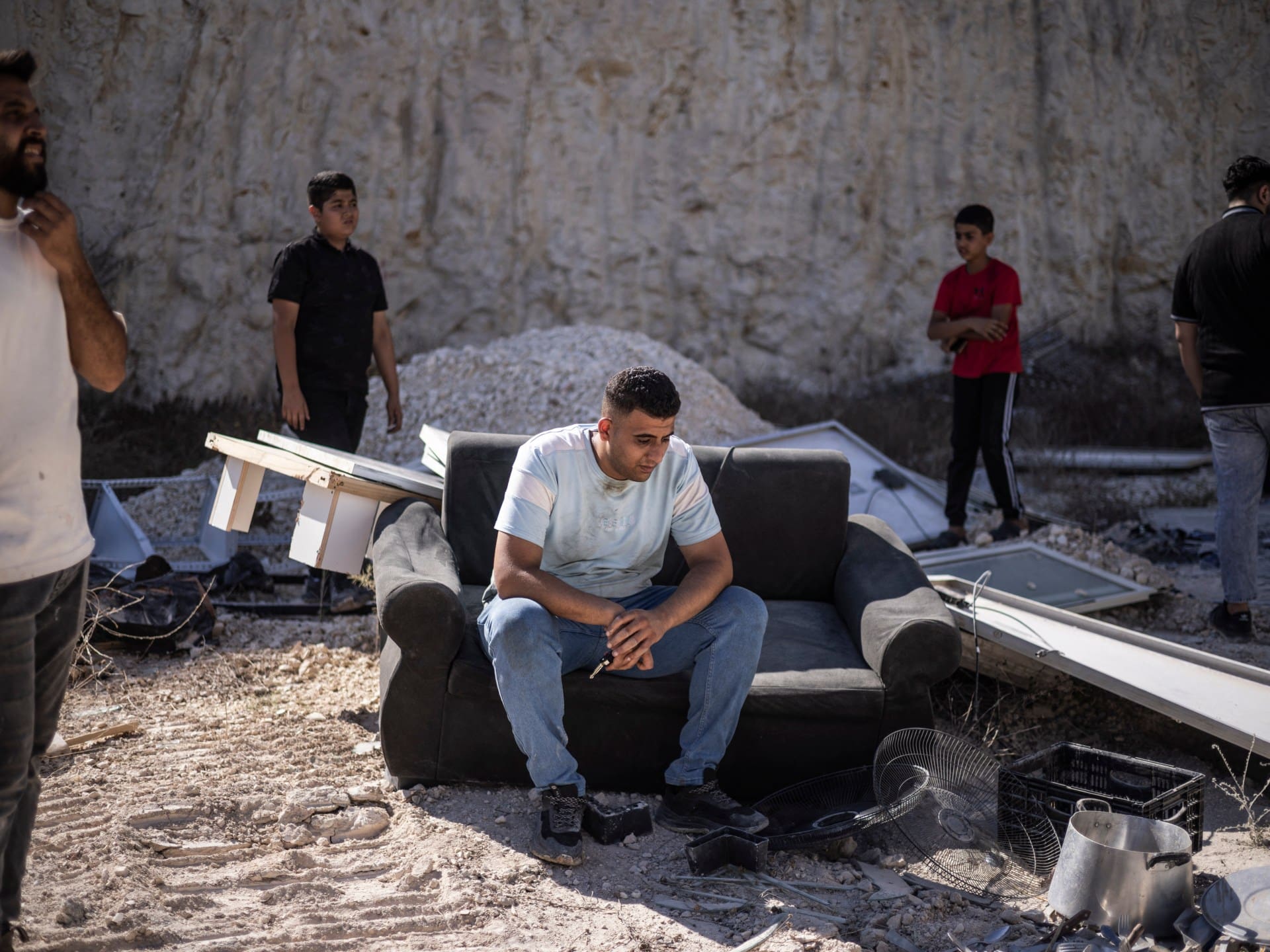 A Palestinian man sits on a couch in front of a building containing shops and flats that were demolished by Israeli forces, citing the lack of a building permit, in Anzah, south of the Palestinian city of Jenin in the northern Israeli-occupied West Bank, on July 27, 2026.