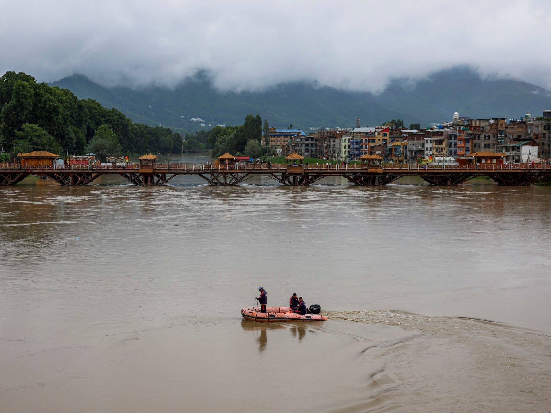 Members of Jammu & Kashmir Police patrol in a boat past a wooden bridge across the overflowing Jhelum River following heavy rain, in Srinagar, Indian Kashmir, July 24, 2026. REUTERS/Sharafat Ali